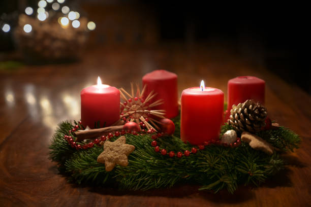 Second Advent - decorated Advent wreath from fir branches with red burning candles on a wooden table in the time before Christmas, festive bokeh in the warm dark background, copy space, selected focus